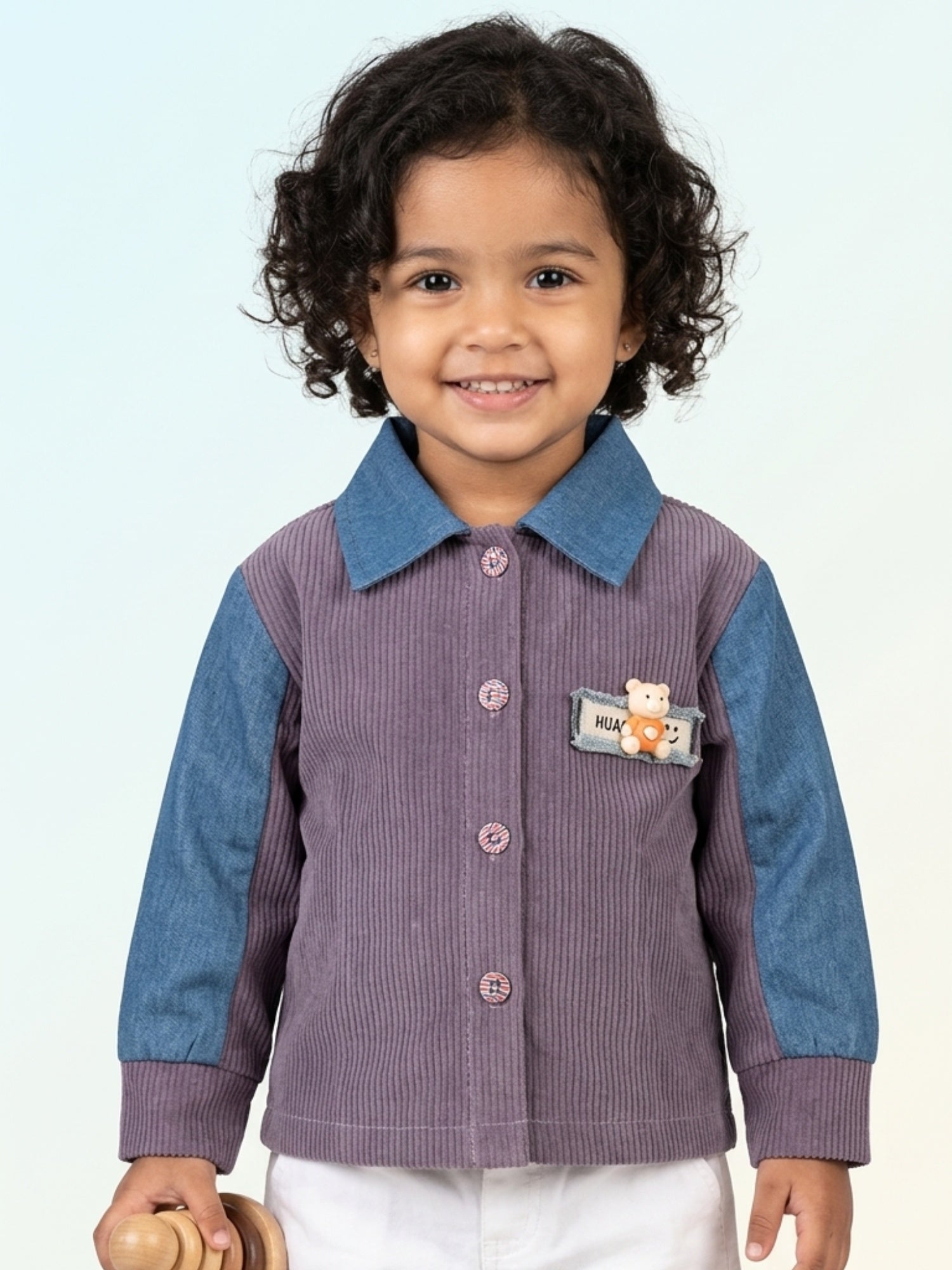 Young child wearing a purple ribbed corduroy button-down shirt with blue denim sleeves and a small teddy bear accent on the chest.