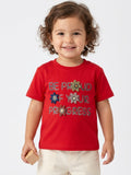 Toddler girl wearing a bright red short-sleeve t-shirt with "Be Proud Of Your Progress" text and felt flower accents.