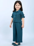 Little girl wearing a two-piece teal textured co-ord set with ruffle sleeves, button-down shirt, and wide-leg trousers against a light blue background