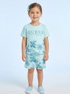a young girl wears a mint green short-sleeve t-shirt with "GUESS Los Angeles" branding and a blue-toned palm tree graphic, paired with matching printed shorts.