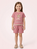a smiling young girl wears a dusty onion pink short-sleeve t-shirt featuring a matching floral appliqué and scalloped lace trim along the hem and cargo pockets.