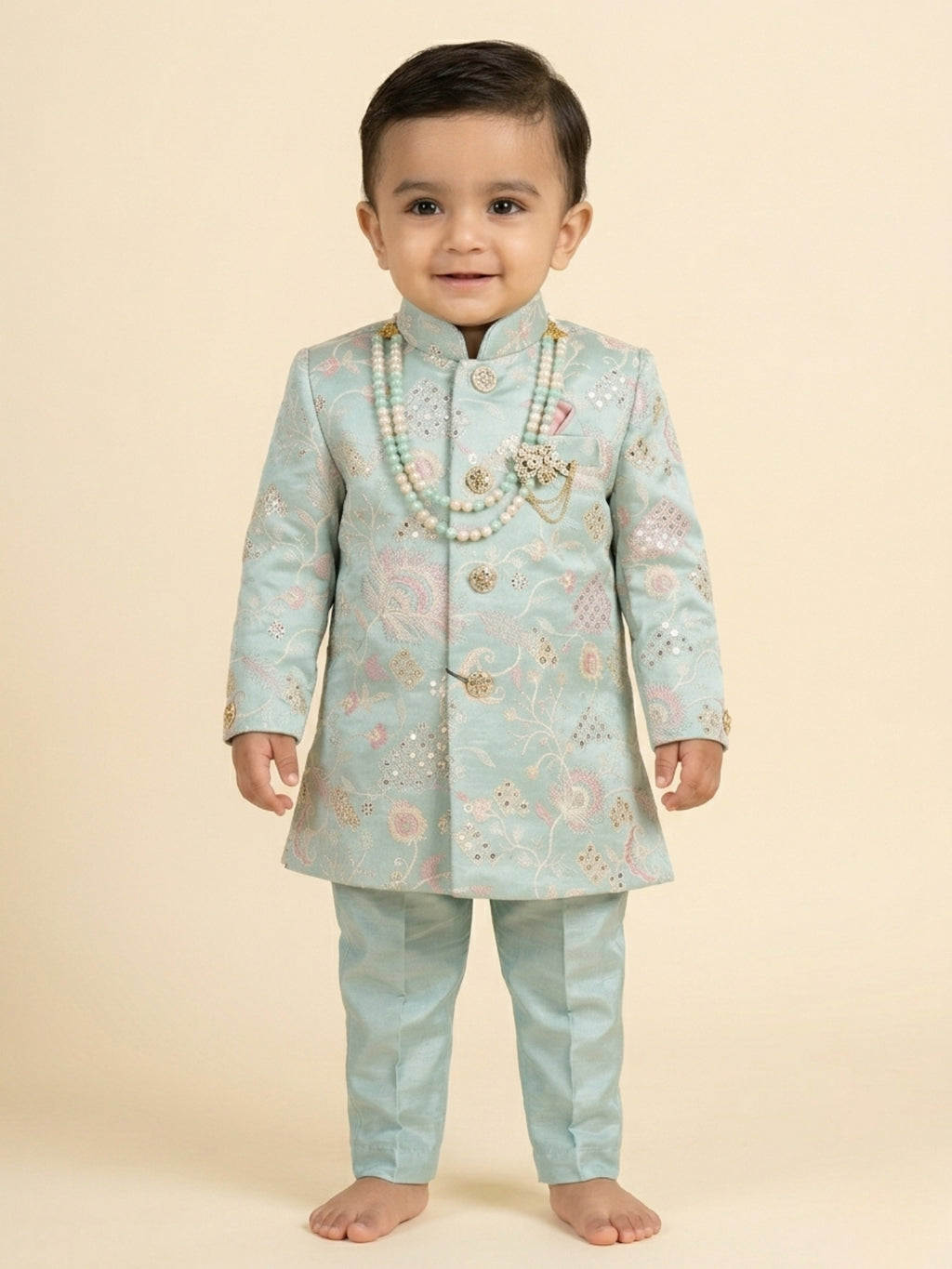 Toddler boy wearing a mint green embroidered sherwani with traditional dhoti and pearl necklace.