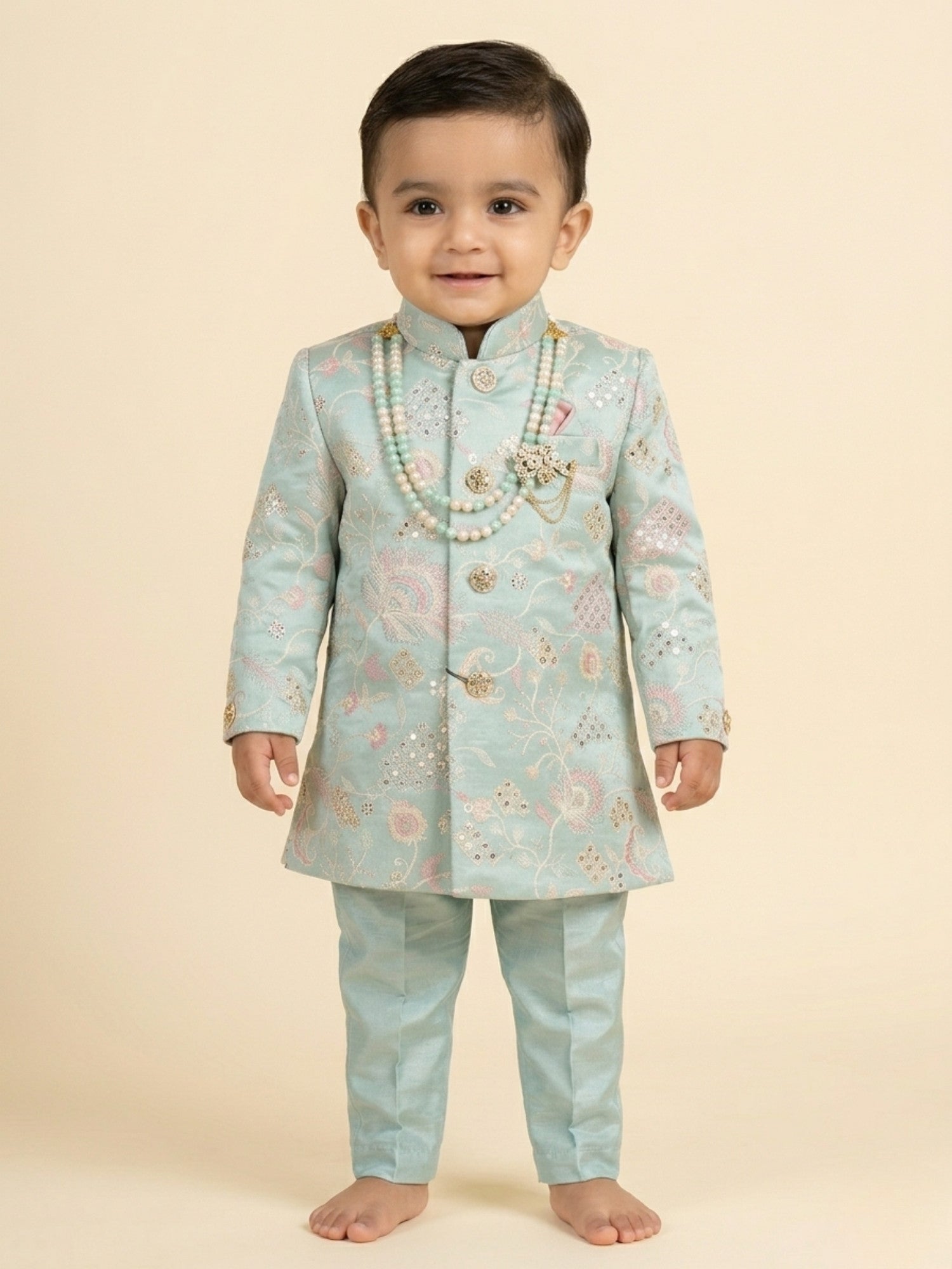 Toddler boy wearing a mint green embroidered sherwani with traditional dhoti and pearl necklace.