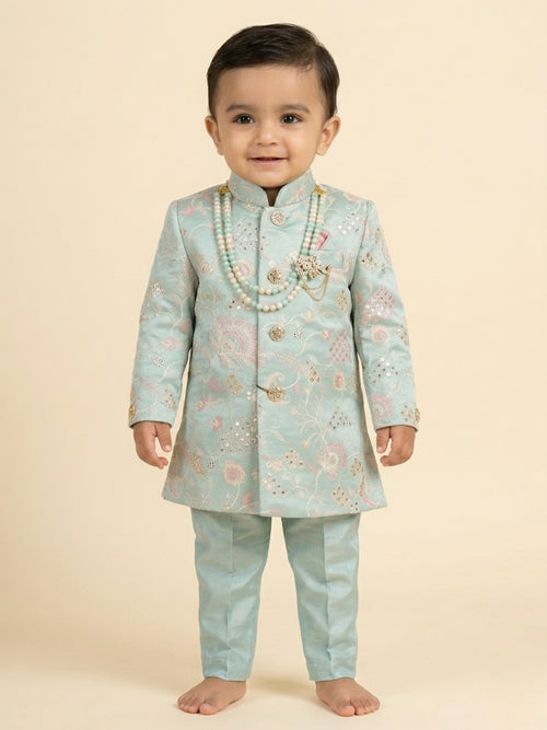 Toddler boy wearing a mint green embroidered sherwani with traditional dhoti and pearl necklace.