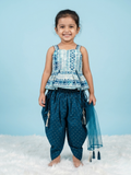 Little girl smiling in a teal blue ethnic outfit featuring a blue and white geometric print peplum top, dark teal dhoti pants with gold dots, and a sheer net dupatta.