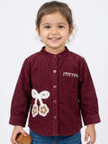 Little girl in a wine red ribbed corduroy shirt featuring a large white crochet bow and cherry-style floral accents