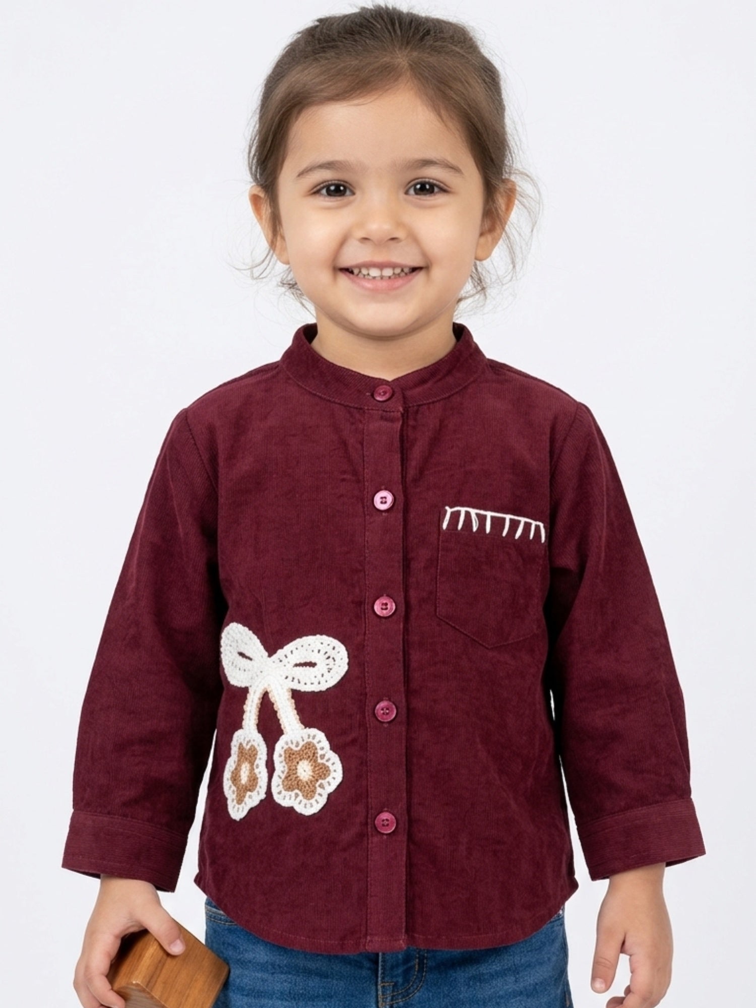 Little girl in a wine red ribbed corduroy shirt featuring a large white crochet bow and cherry-style floral accents