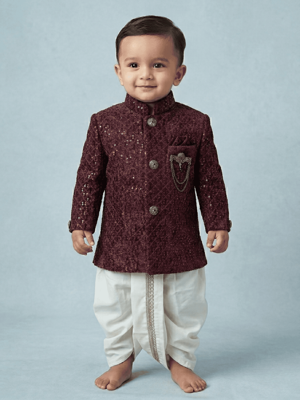 Little boy wearing a maroon sequin velvet sherwani with a traditional cream dhoti.