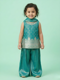 A young girl wearing a teal blue sleeveless Banarasi silk kurti with an embroidered neckline and matching flared sharara pants against a mint green background.