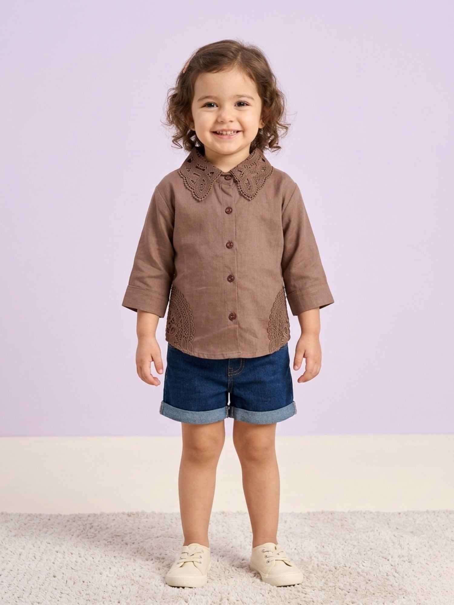 A young girl smiling while wearing a mocha brown long-sleeve button-down blouse featuring a large, intricate lace Peter Pan collar and matching lace side-panel accents.