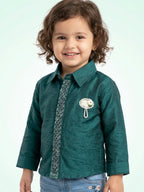 Little girl in a rich emerald green silk-finish shirt with an intricately beaded center strip and a pearl floral brooch