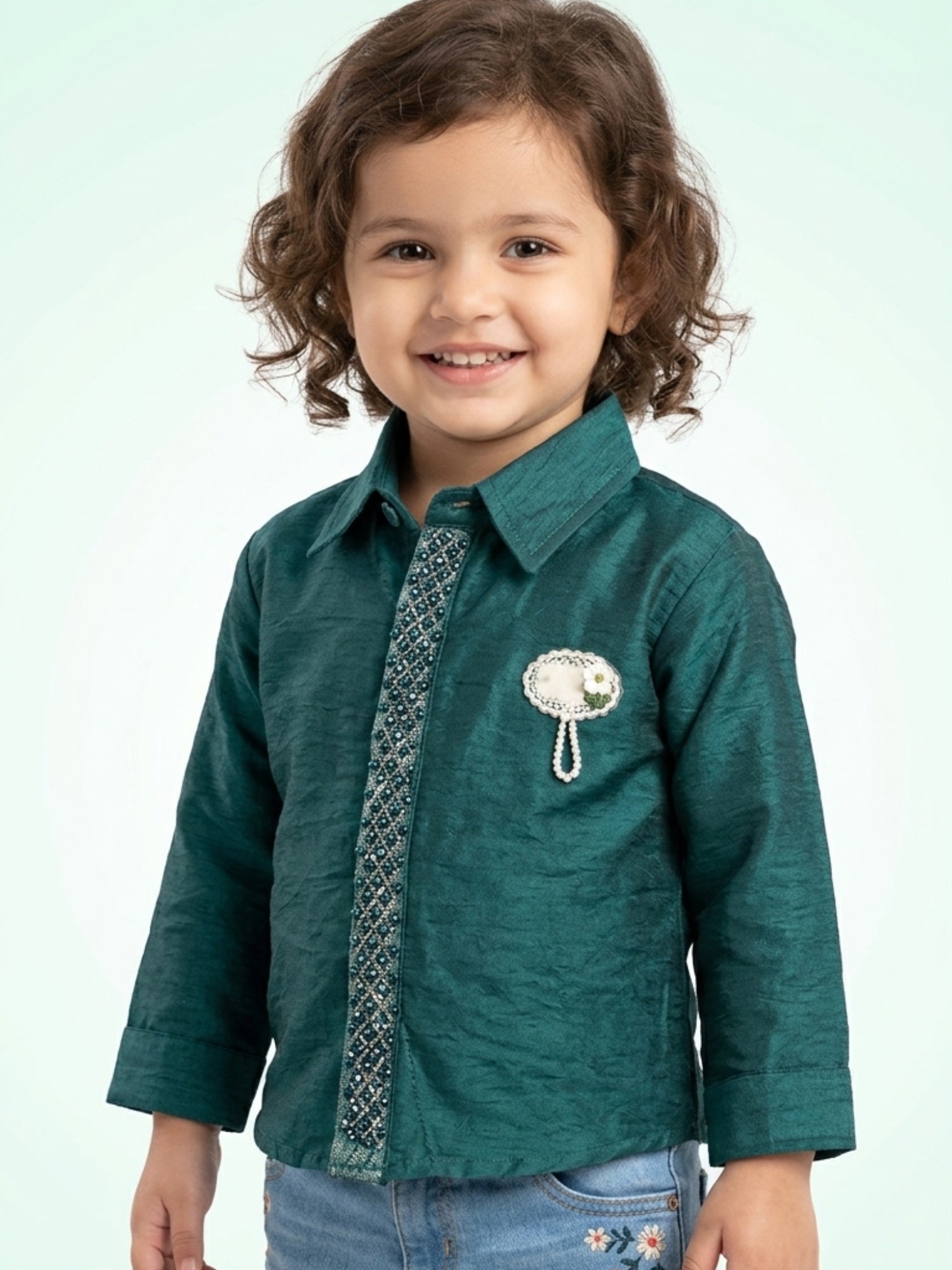 Little girl in a rich emerald green silk-finish shirt with an intricately beaded center strip and a pearl floral brooch