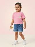 A young girl wearing a bright bubblegum pink short-sleeve tee with a "Reach for the Stars" patch on the chest, paired with embroidered denim shorts.