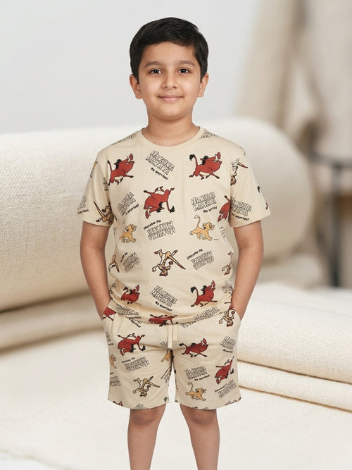 Young boy with hands in pockets wearing a beige two-piece cotton set with an all-over Lion King character print featuring Simba and Pumbaa.
