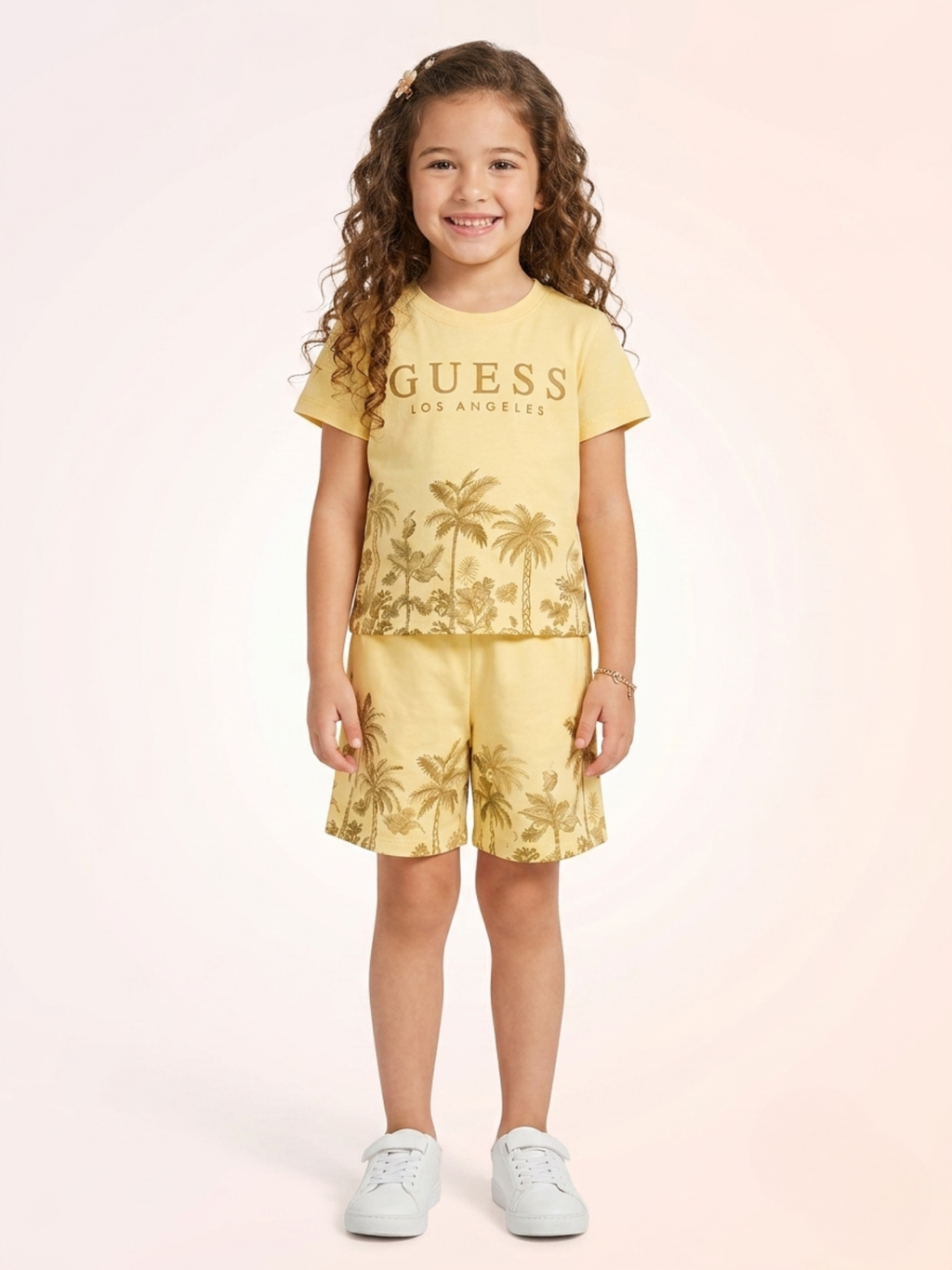 a young girl with long curly hair wears a soft yellow knit t-shirt and elastic-waist shorts set featuring golden-brown palm tree landscape graphics.