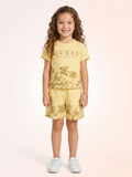 a young girl with long curly hair wears a soft yellow knit t-shirt and elastic-waist shorts set featuring golden-brown palm tree landscape graphics.