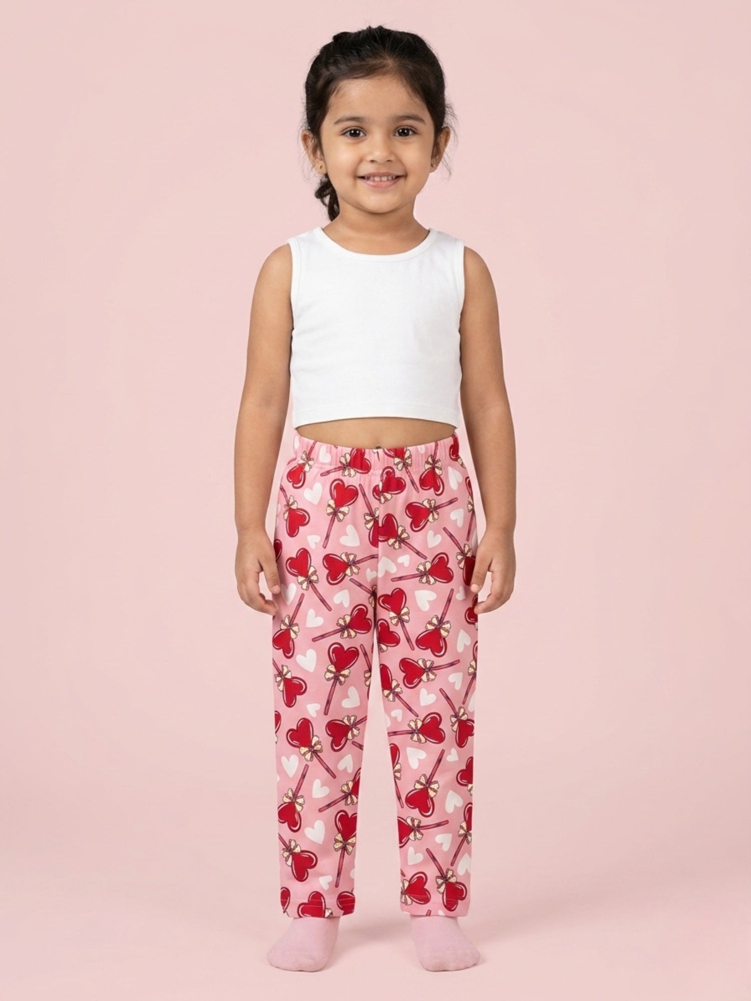 Girl wearing bright pink cotton pajama pants with a repeating red heart lollipop and white heart pattern.