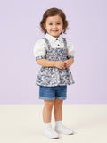 A toddler girl wearing a white short-sleeve puff-sleeve blouse with a built-in blue and white floral smocked bodice overlay, paired with denim shorts.