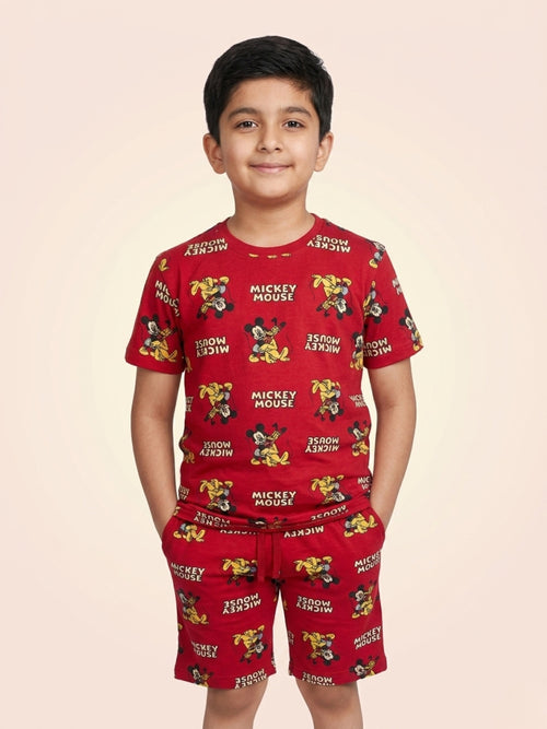 Young boy smiling with hands in pockets wearing a bright red two-piece cotton set with an all-over Mickey Mouse character and text print.