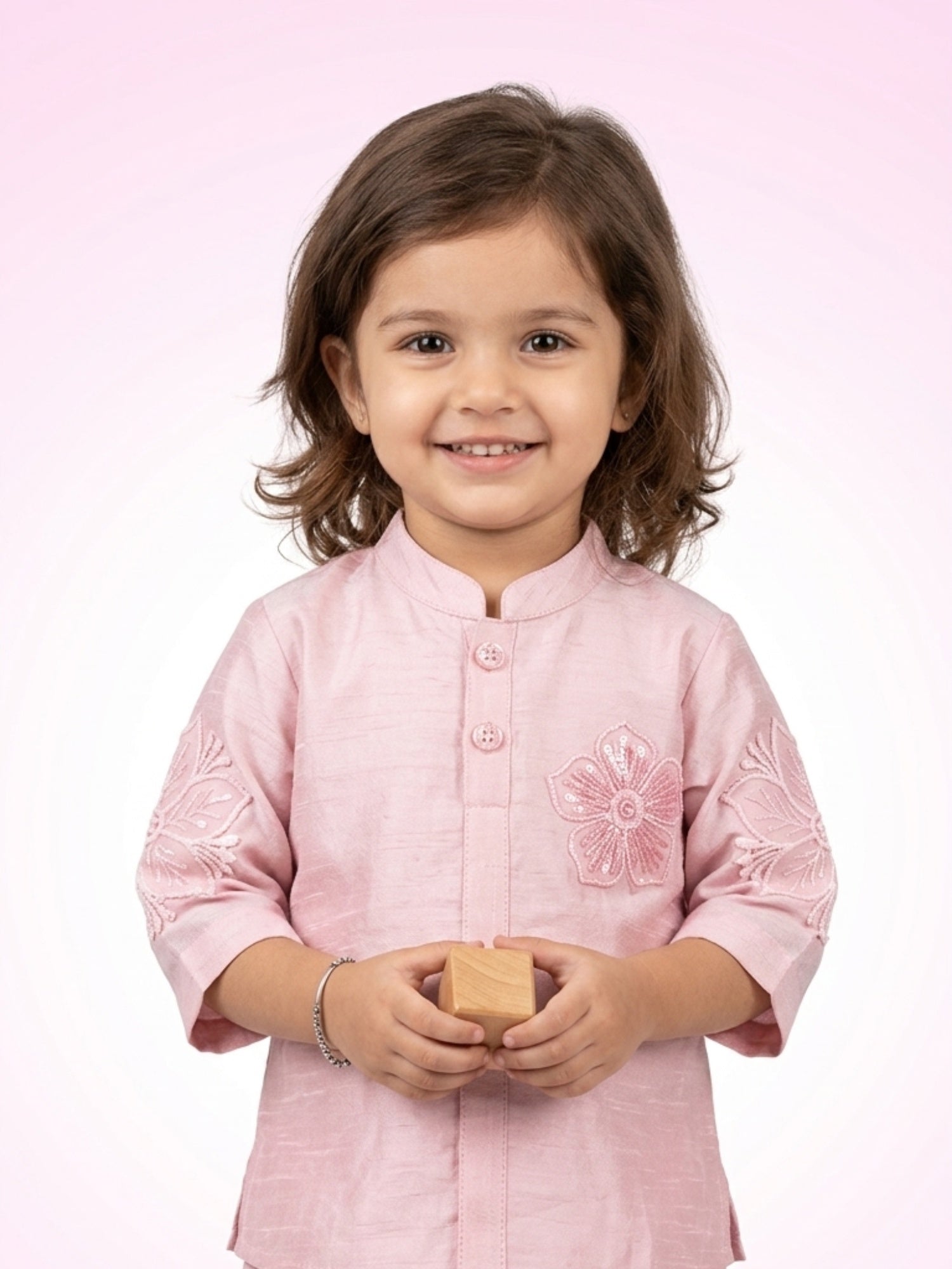 Little girl in a blush pink silk kurta featuring a large floral applique on the chest and embroidered sleeve details.