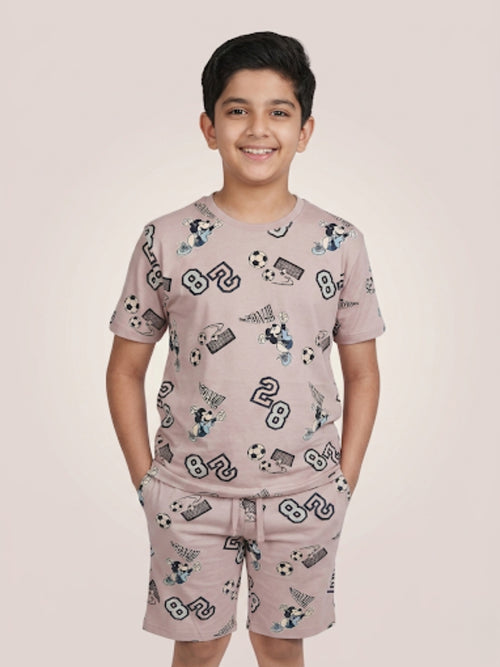 Young boy smiling with hands in pockets wearing a mauve two-piece cotton set with an all-over football-themed Mickey Mouse and soccer ball print.